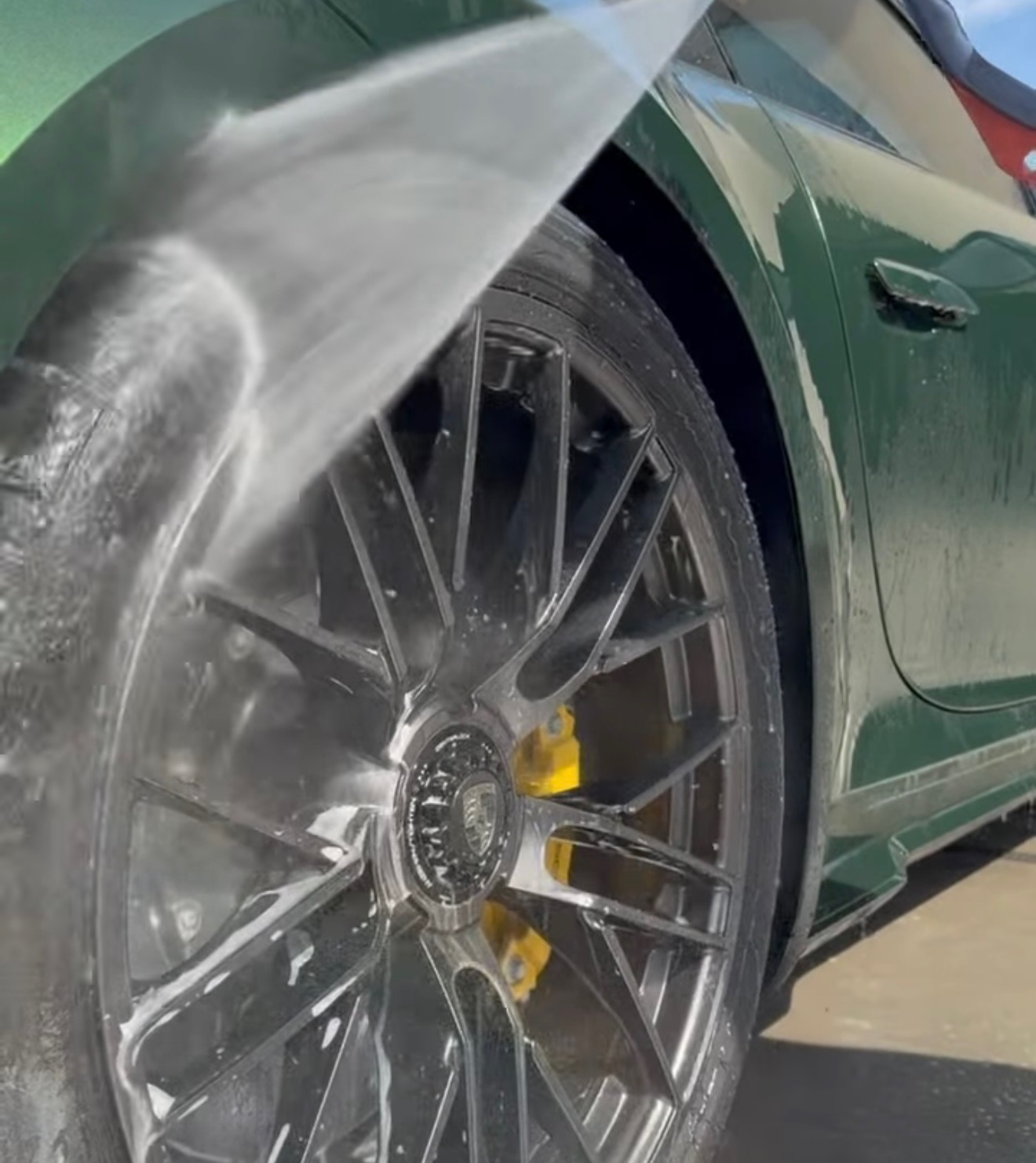 Green Porsche wheel being rinsed during a mobile detail